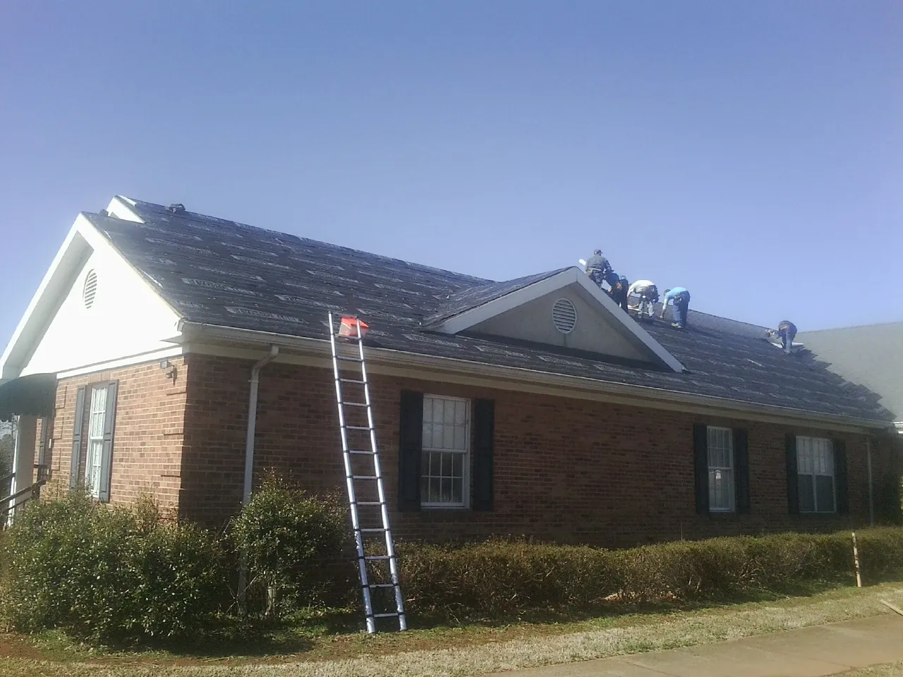 Crew tearing shingles off a brick ranch roof with a ladder set — Emergency Roof Repair work by our crew in Medina