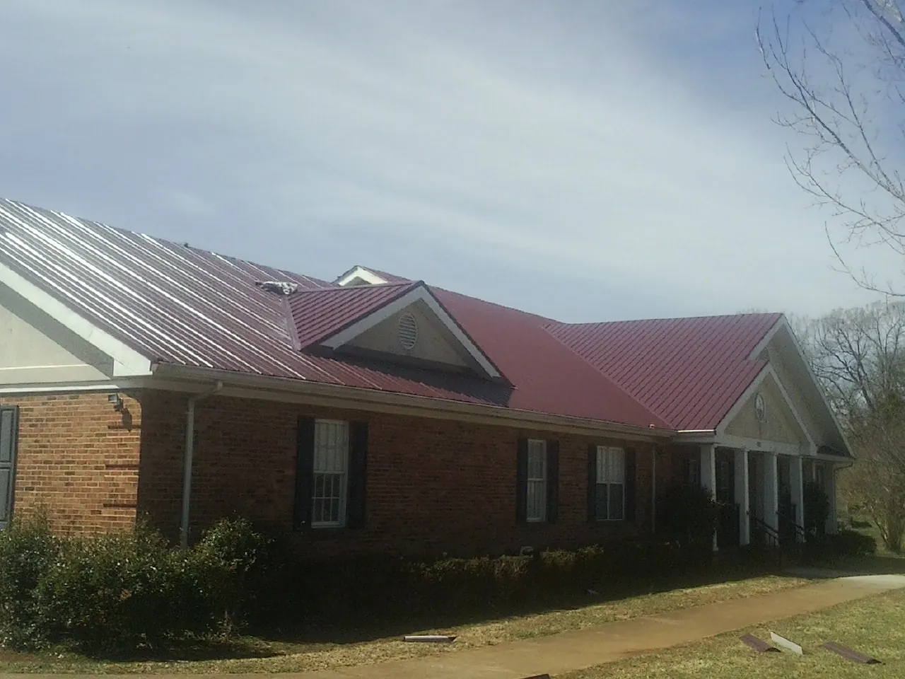 Red metal roof with gabled entries on a long brick building, from a Hail Damage Roof Repair job in Medina